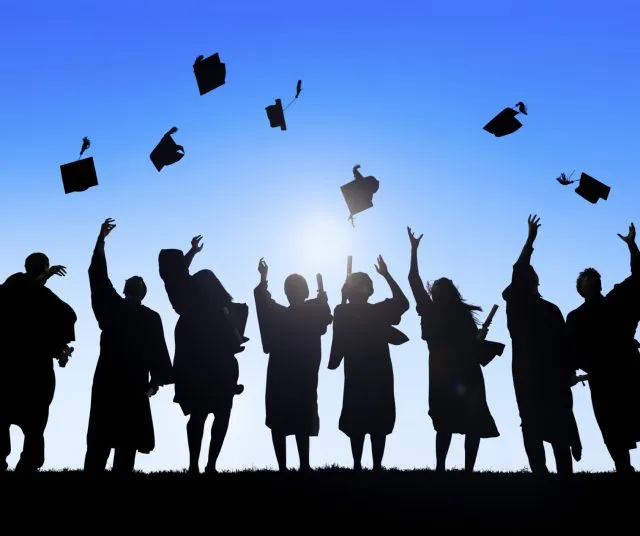 Silhouette of students celebrating their graduation by throwing their hats into the air
