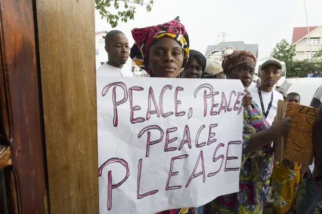 People of the DRC holding a sign saying Peace, Peace, Peace, Please