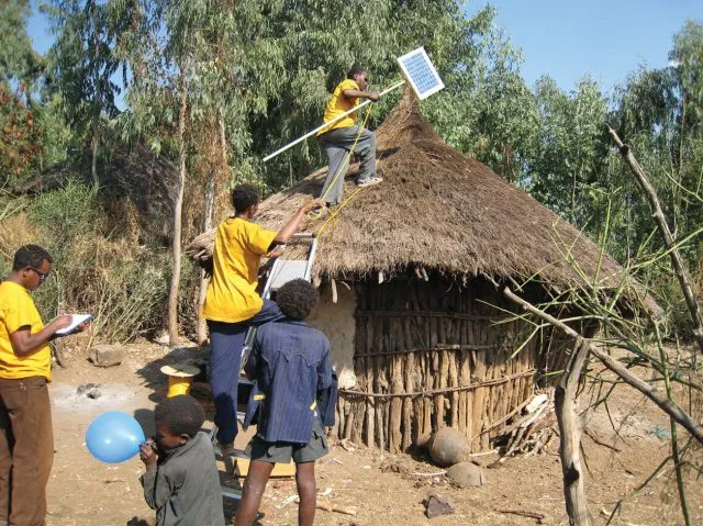 Men fitting a solar panel to the roof of a shack in Ethiopia
