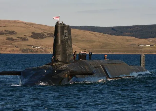Trident submarine with military personnel stood atop with land in the background
