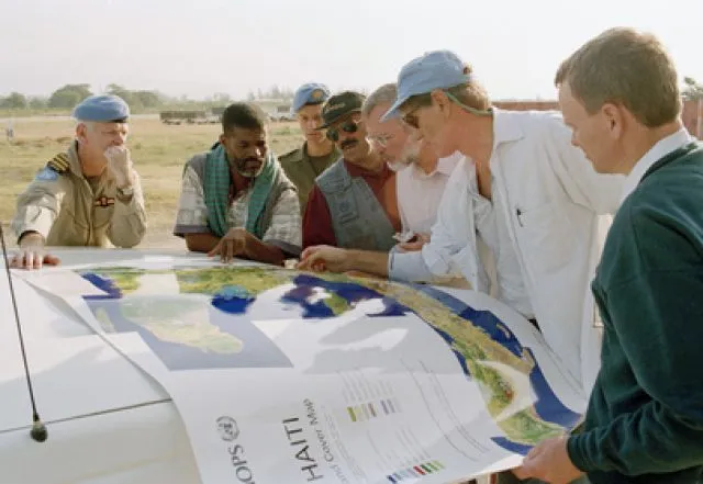 Seven men looking over a map of Haiti on the bonnet of a vehicle