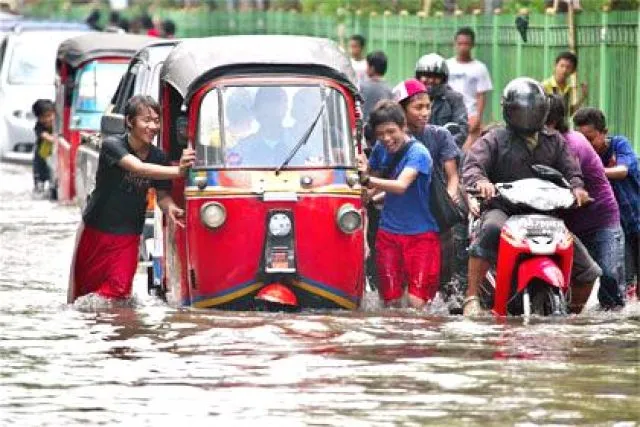 People pushing a red rickshaw through flooded streets