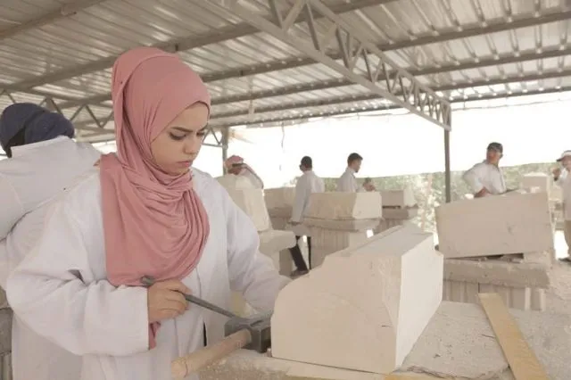 Woman wearing headscarf using tools to carve white stone