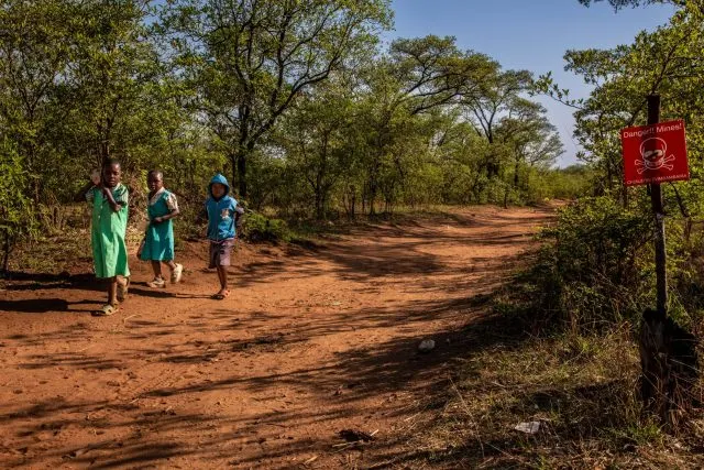 A group of children in Zimbabwe walk along a path near a sign warning of landmines