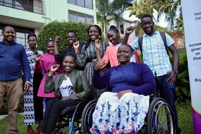 A group of young people with disabilities from Show Abilities Uganda smile at the camera & hold up their fists in a symbol of power