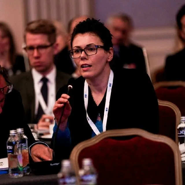 Image shows Ľubica Polláková speaking into a microphone at a conference.